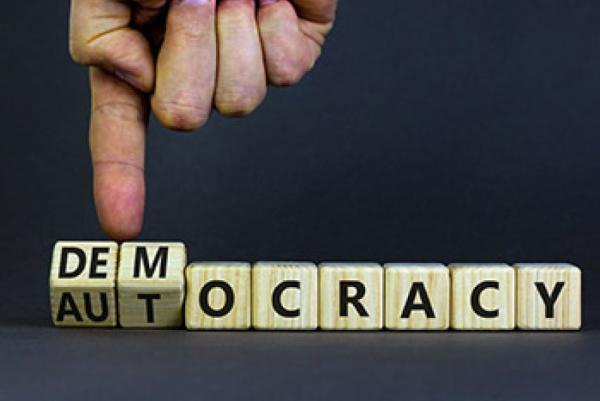 Hand turning over letters to spell Democracy or Autocracy